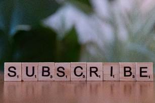 scrabble letters spell out SUBSCRIBE on a table top with a blurry background.